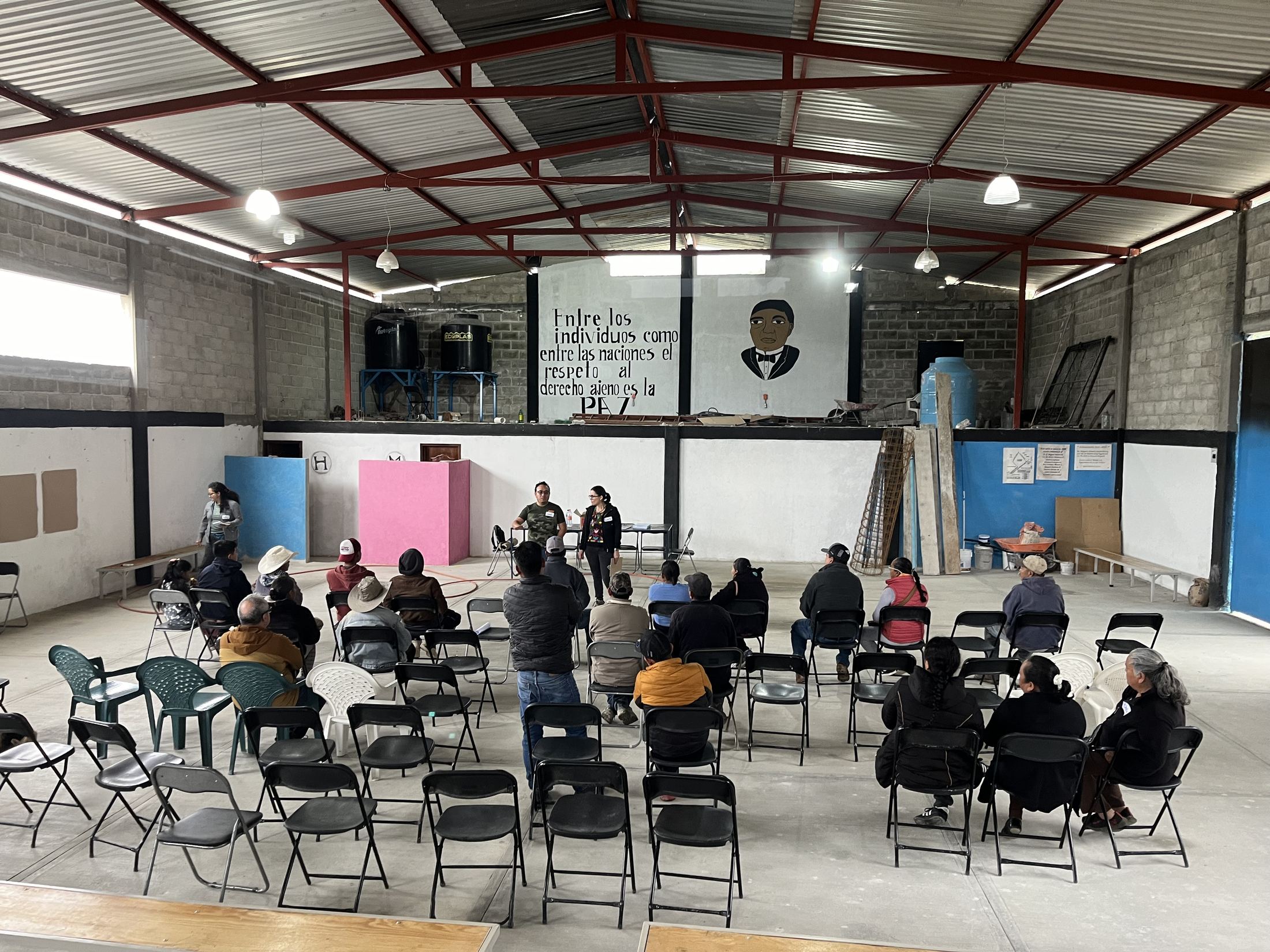 Asamblea comunitaria en un salón con un mural sobre derechos colectivos